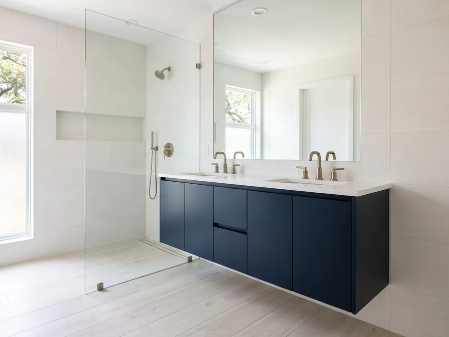 Remodeled primary bathroom with a navy floating vanity and a glass shower panel